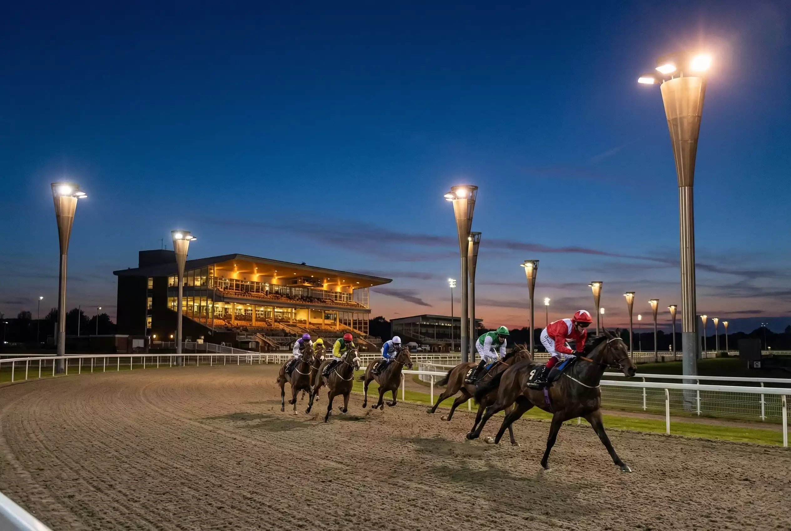 Chelmsford City Racecourse under floodlights with horses racing on Polytrack surface